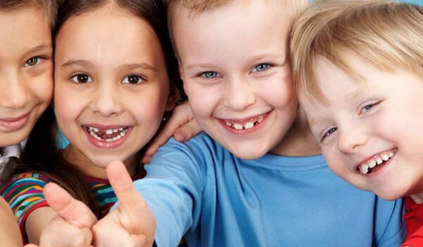 Four children smiling at the camera with thumbs up