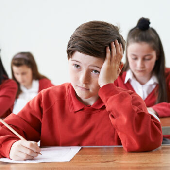 Boy at school in red jumper looking bored