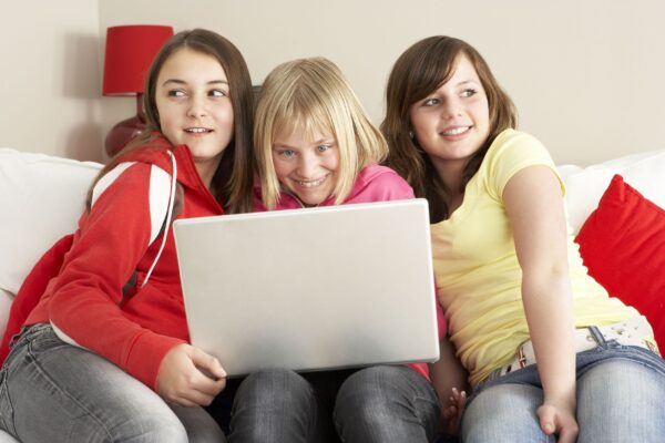 Three sisters on a couch and using a laptop at home