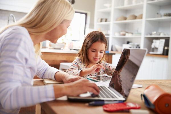 mother and young daughter at kitchen table on ipad and laptop