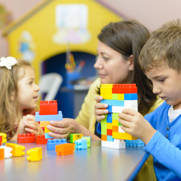 Children in a classroom with teacher playing with plastic building blocks