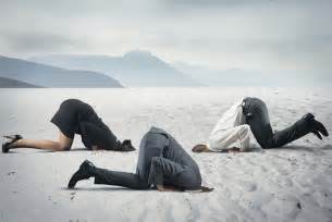 Business people in a dessert with their heads in the sand