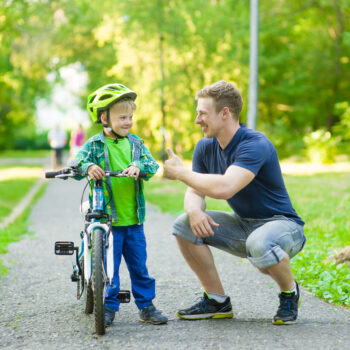 Father teaching a boy to ride a bike and giving him the thumbs up