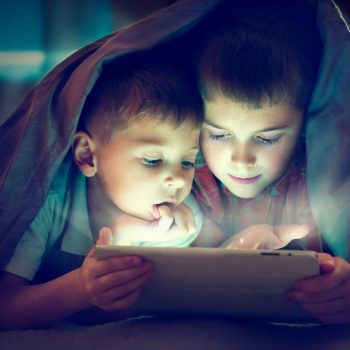 Children playing with a tablet at night under the covers