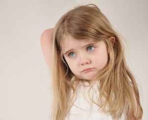 A little child looks sad and frustrated. The girl has her hand over her head for a parenting or tired concept.